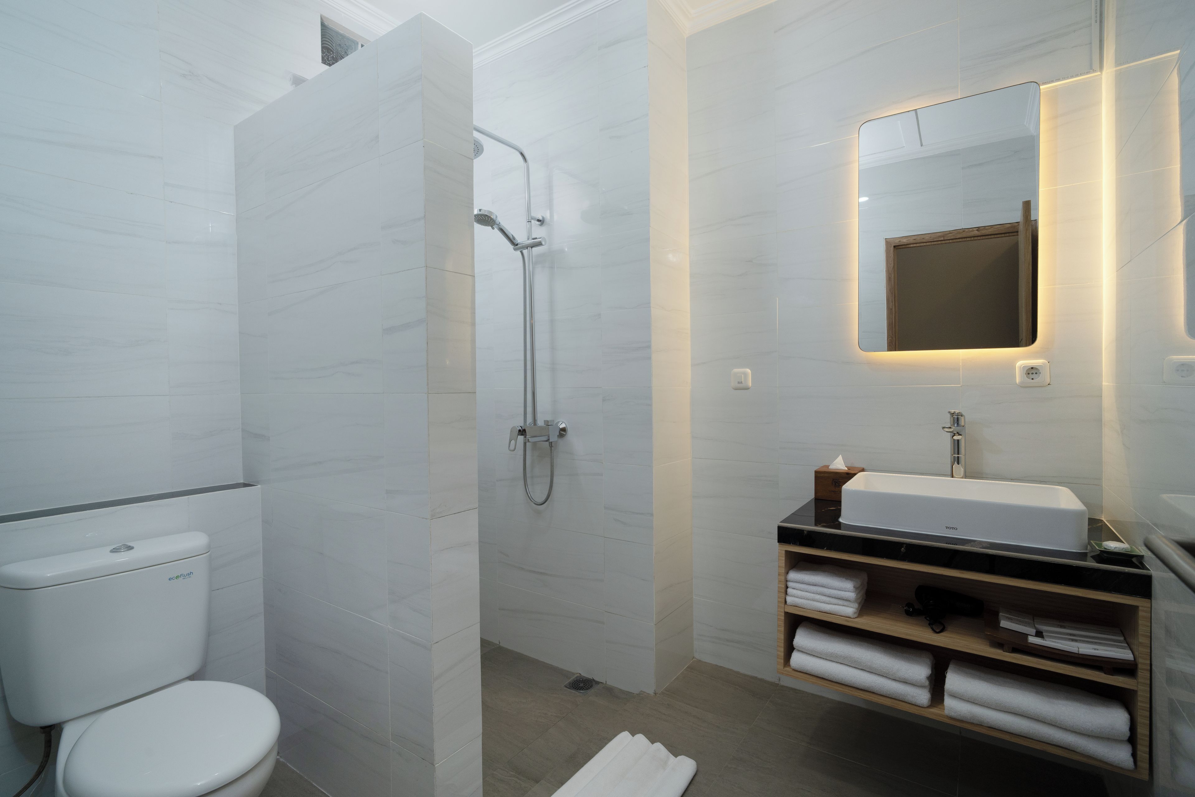 Un baño moderno con inodoro, ducha, lavabo y espejo con iluminación integrada.