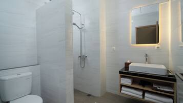 Un baño moderno con inodoro, ducha, lavabo y espejo con iluminación integrada.