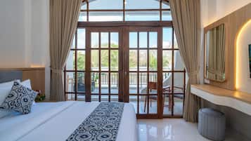 A bedroom with a large bed, a desk, a chair, a mirror, and a view through a glass door to an outdoor area.