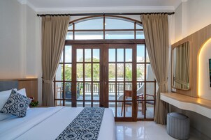 Un dormitorio con una cama grande, un escritorio, una silla, un espejo y vistas al exterior a través de una puerta de cristal.