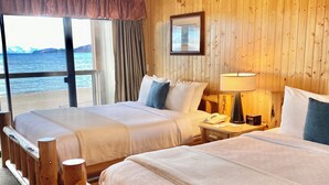 Habitación de hotel con dos camas, cabeceros de madera, un ventanal con vistas al mar y un cuadro en la pared.
