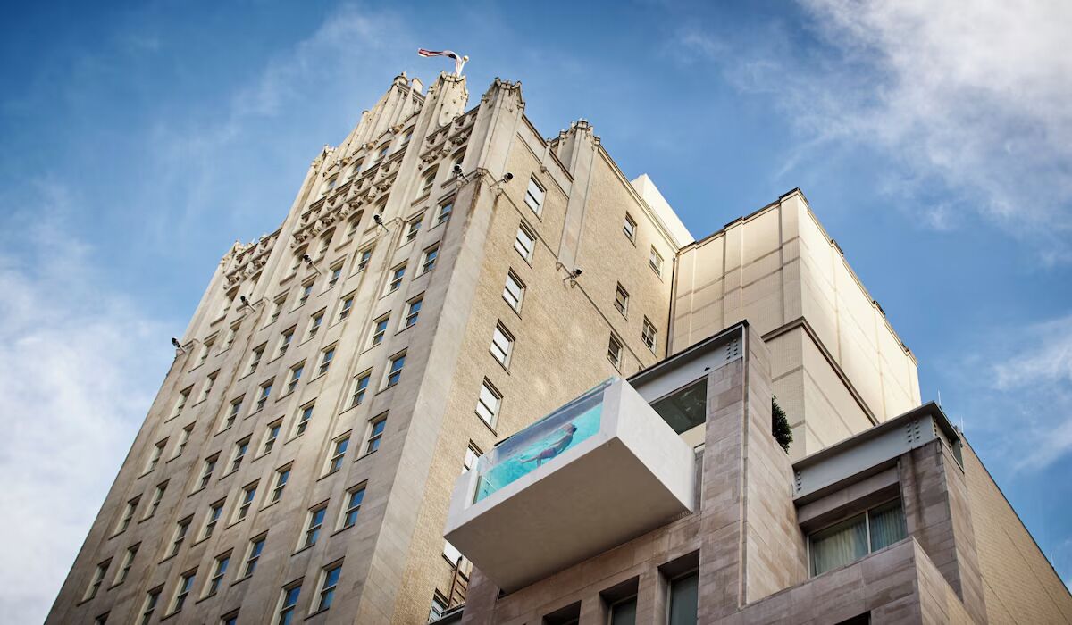 A tall building with a modern architectural design, featuring multiple windows and a prominent balcony with a view.