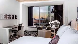 Een hotelkamer met een bed, een bureau, een stoel, een bank, een groot raam met uitzicht over de stad en een zwarte lamp.