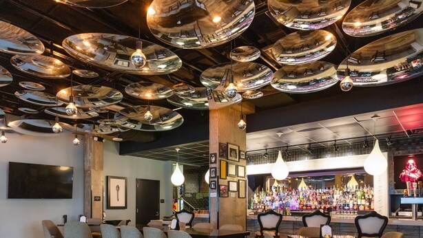 A bar area with multiple hanging mirrors, a bar counter with bottles, and seating with tables and chairs.