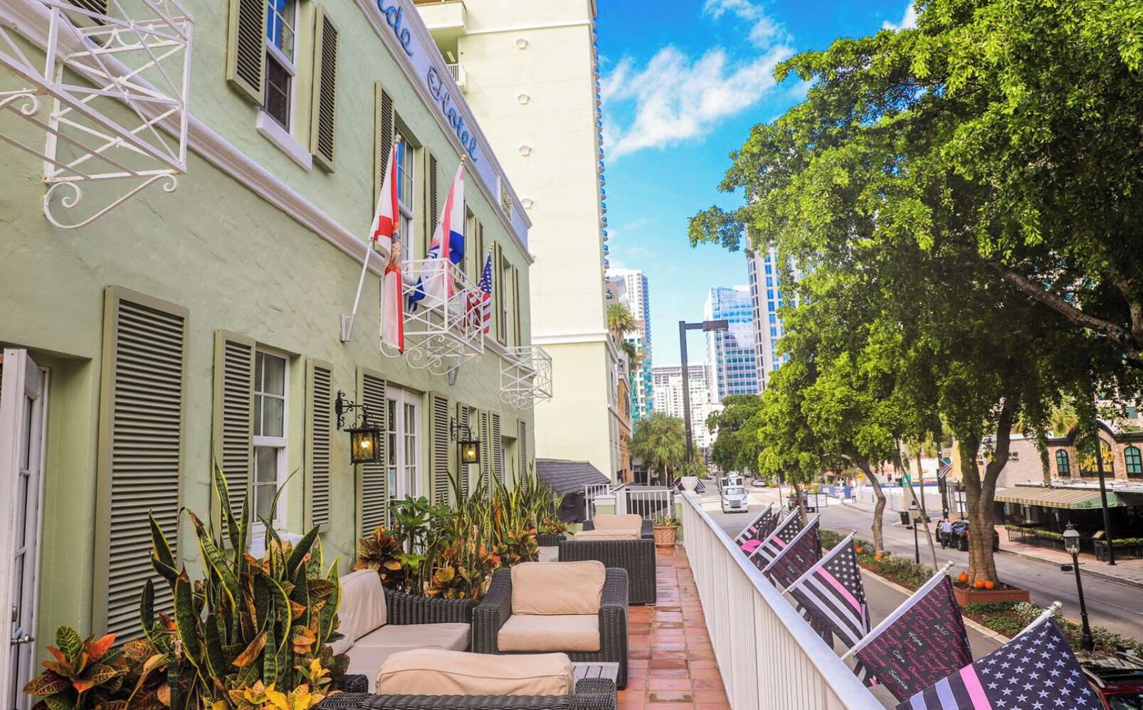 A hotel with outdoor seating, flags, and a view of the street.