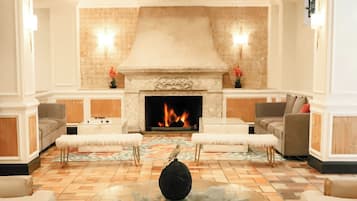 Un hall espacioso con chimenea, dos sofás, una mesa redonda con un jarrón decorativo y una alfombra estampada.