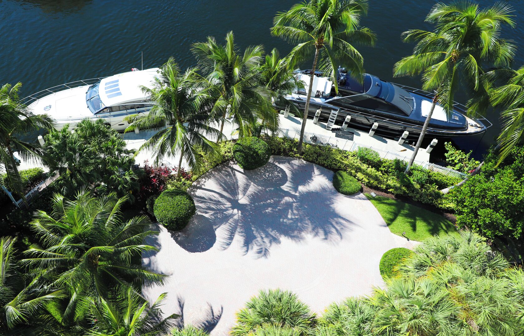 A yacht docked at a marina with palm trees and a landscaped area.