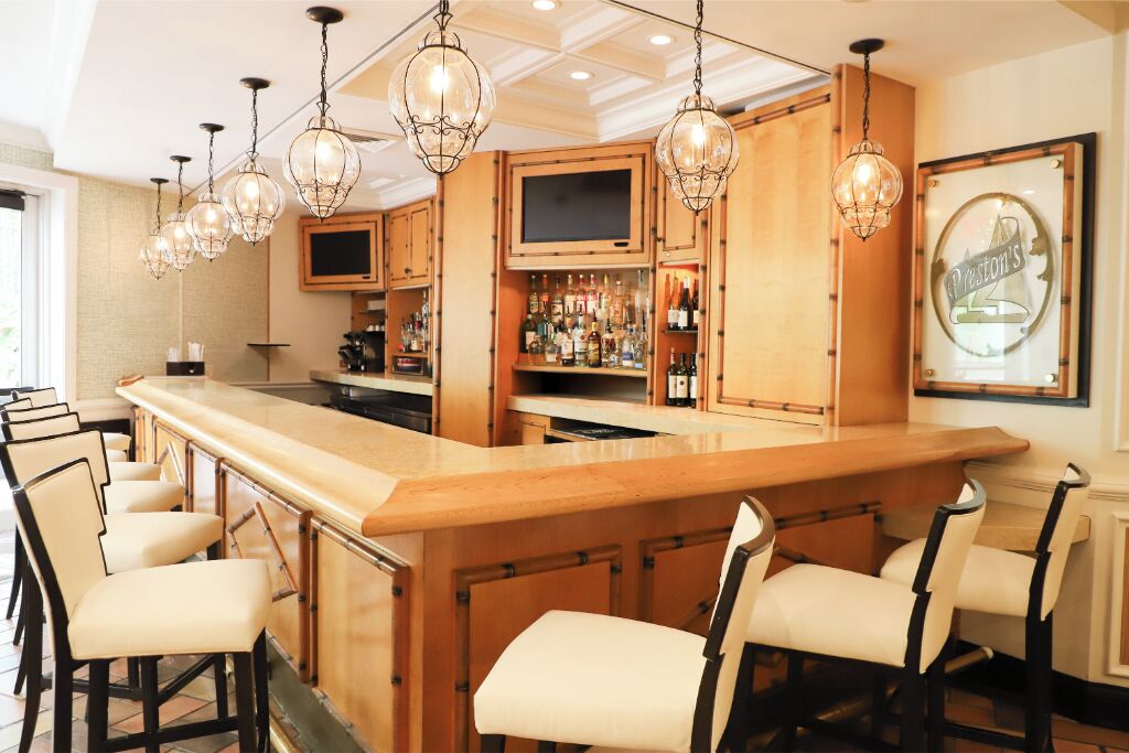 A bar area with a long counter, multiple bar stools, and hanging light fixtures.