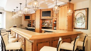 A bar area with a long counter, multiple bar stools, and hanging light fixtures.