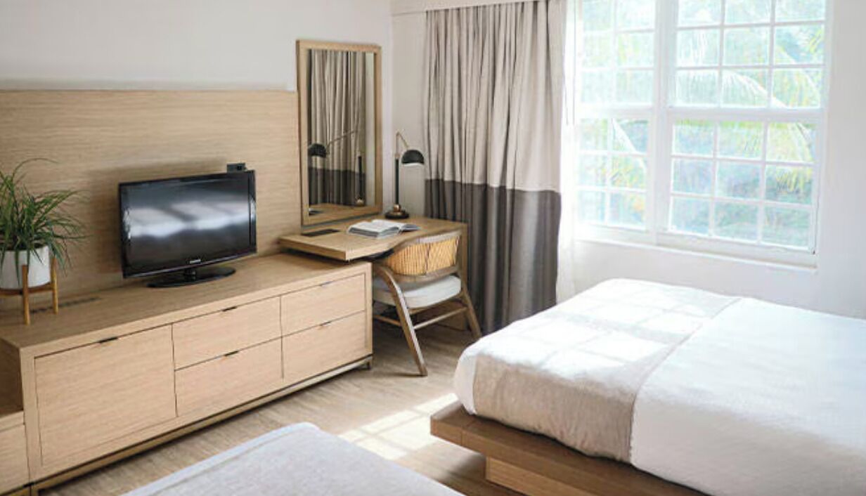 Habitación de hotel con cama, televisor, escritorio con silla, espejo y ventana con cortinas.