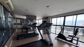 A gym with treadmills, exercise bikes, and a large window with a city view. - Residencial Macambira (Campina Grande)