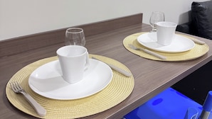 A dining table set with white plates, cups, and cutlery, accompanied by woven placemats. - Residencial Macambira (Campina Grande)