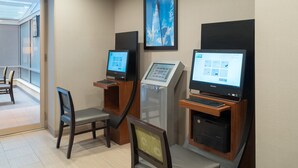 Un vestíbulo de hotel con mostrador de recepción, quiosco de autoservicio y estación de computadoras.