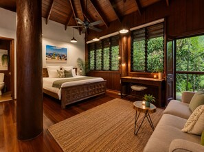 A bedroom with a bed, a desk, a chair, a large window with a view of greenery, and a ceiling fan.