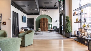 Um interior moderno com piso de madeira, uma poltrona verde, um sofá, uma mesa redonda e uma estante com garrafas.