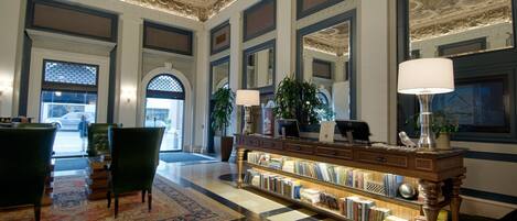 A lobby with a grand ceiling, a reception desk, a bookshelf, and a large window.