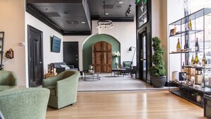 A modern interior with a wooden floor, a green armchair, a sofa, a round table, and a bookshelf with bottles. - 2 Double Beds | Sentinel | Group Base, Downtown West End, Historic Charm (Portland)