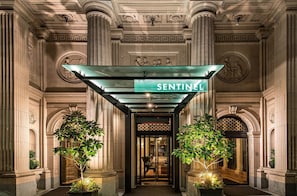 A grand entrance with a sign reading 'SENTINEL' above a glass door, flanked by columns and decorative ceiling. - Sentinel | Executive King | Historic Luxury, Curated Art, Wine Lounge (Portland)