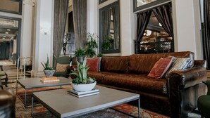 A living room with a brown leather sofa, a coffee table with a plant, and a patterned rug. - Sentinel | Executive King | Historic Luxury, Curated Art, Wine Lounge (Portland)