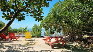 A beach setting with a wooden picnic table, two red chairs, and a yellow chair.