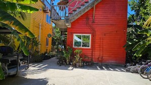 A red building with a staircase, a yellow building, and a thatched-roof structure.