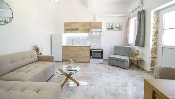 A modern living room with a sofa, a glass coffee table, and a kitchen in the background.