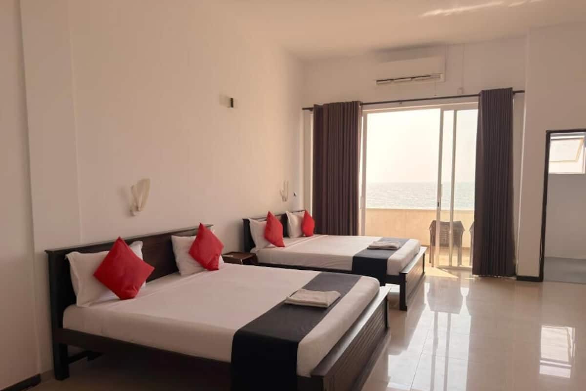 A hotel room with two beds, a balcony with curtains, and a view of the sea.