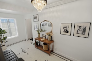 Un pasillo con candelabro, cuadros enmarcados, un espejo, una consola decorada con objetos y un tapete estampado.