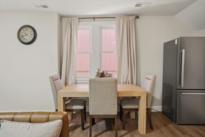 A dining area with a wooden table, four chairs, a clock on the wall, and a refrigerator. - Four Tops Suite  Renovated 2BR/2BA Midtown (Detroit)