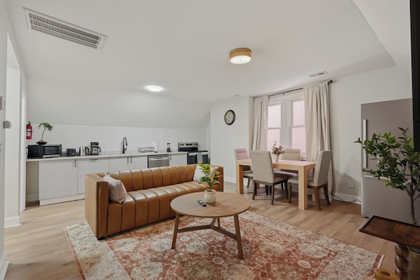 Un espacio habitable compacto con kitchenette, un sofá, una mesa de comedor con sillas y una pequeña mesa de centro.