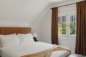 A hotel room with a bed, a nightstand, a lamp, and a window with curtains.