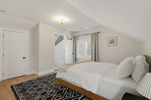 A bedroom with a bed, a patterned rug, a door, and a staircase leading to another room. - Four Tops Suite  Renovated 2BR/2BA Midtown (Detroit)