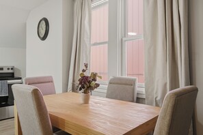 A dining area with a wooden table, four chairs, a potted plant, and a wall clock.