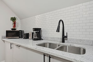 Una cocina con encimera de granito, pileta de acero inoxidable, cafetera, tostadora y microondas.