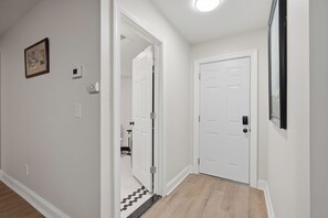 A hallway with two white doors, a small framed picture on the wall, and a thermostat on the wall.