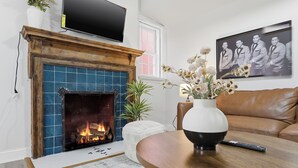 Un salon avec une cheminée, un téléviseur fixé au-dessus, une photographie encadrée accrochée au mur et un canapé en cuir marron.