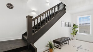 Un escalier avec une main courante et des marches en bois foncé, une plante en pot, un banc et une enseigne murale.