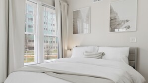 Une chambre à coucher avec un lit, des rideaux, une fenêtre avec des stores et des œuvres d’art murales.