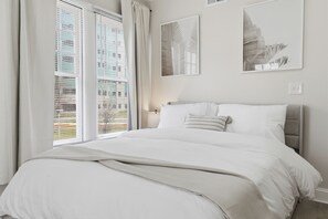 Ein Schlafzimmer mit Bett, Vorhängen, einem Fenster mit Jalousien und Wandbildern.