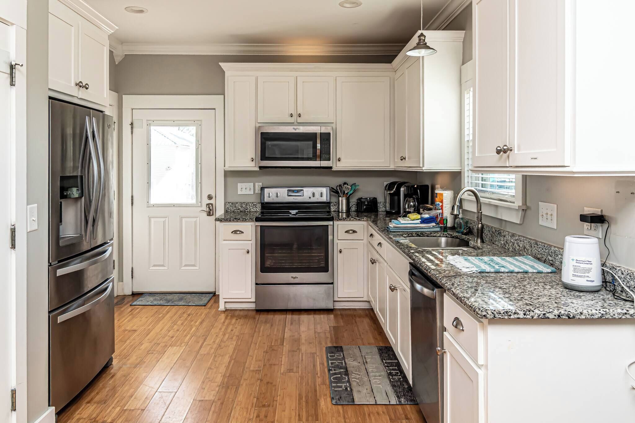 A kitchen with white cabinets, stainless steel appliances, granite countertops, and a window.
