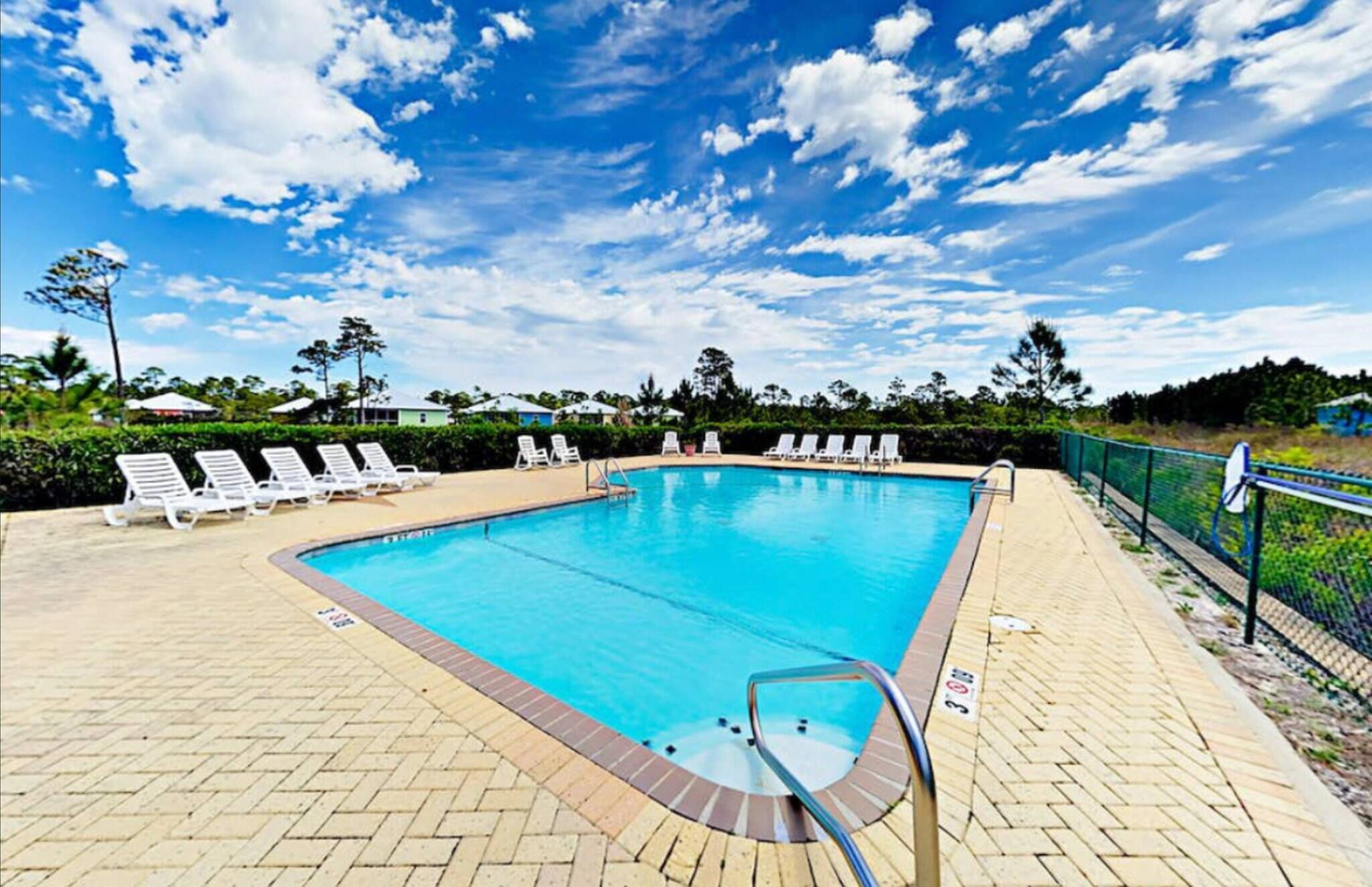 Una piscina rectangular con un borde de baldosas, rodeada de sillas de descanso blancas y una valla.