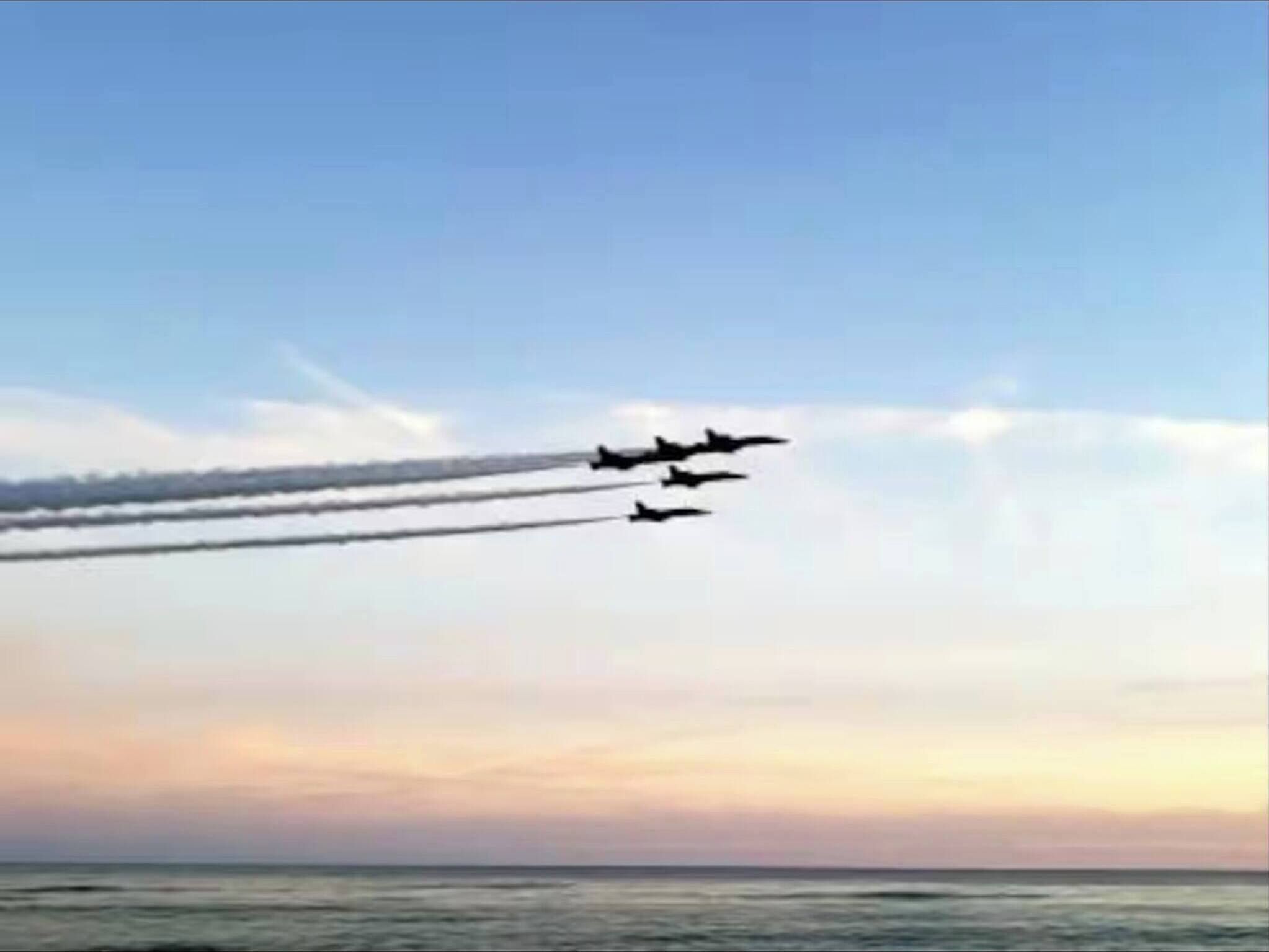 En klar himmel med en solnedgång och en grupp stridsflygplan som flyger i formation.