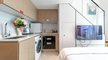 A compact hotel room with a kitchenette, a washing machine, a flat-screen TV, and a bed.