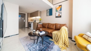 A modern living room with a sofa, coffee table, and yellow armchair. There is a kitchen area with a refrigerator and a microwave. - Hengbang Times Huaqiang North Store (Shenzhen)