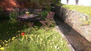 An outdoor seating area with a table and chairs, a brick wall, and a stone wall with a water channel.
