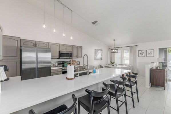 A modern kitchen with stainless steel appliances, a white island with bar stools, and a dining area with a view.
