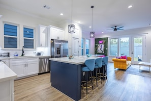A modern kitchen with white cabinets, a central island with bar stools, a stainless steel refrigerator, and a ceiling fan. - 4BR Houston Home - Hot Tub, Outdoor Movies & Karaoke Near NRG/TMC (Houston)