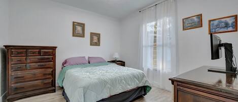 Een slaapkamer met een bed, een houten dressoir, nachtkastje en plafondventilator.