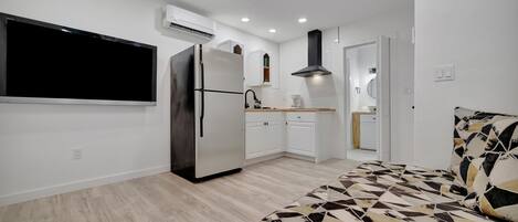 A modern kitchen with a built-in refrigerator, a microwave, and a stove. There is a dining area with a table and chairs. The room has a large window and a bed with a patterned bedspread.