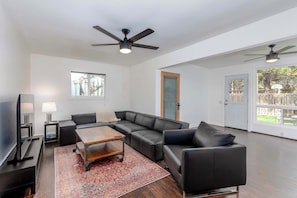 Ein modernes Wohnzimmer mit Ecksofa, Couchtisch, Fernseher und Deckenventilator.